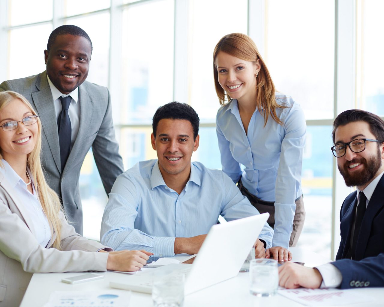 Company of five employees sitting at workplace in office